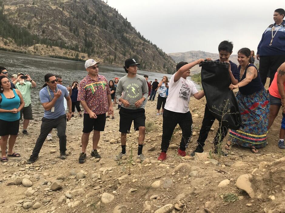 Tribal members lined up passing a bag of salmon toward the water.