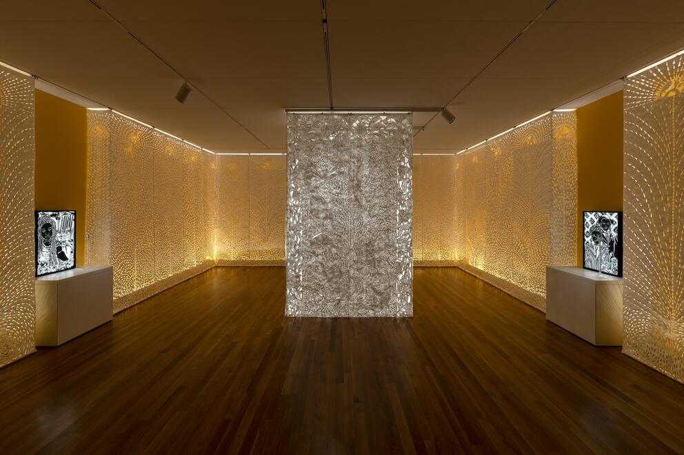 A pillar of paper scrolls cut with symbols in a room clad with intricately cut paper, glowing with a backlit goldon glow