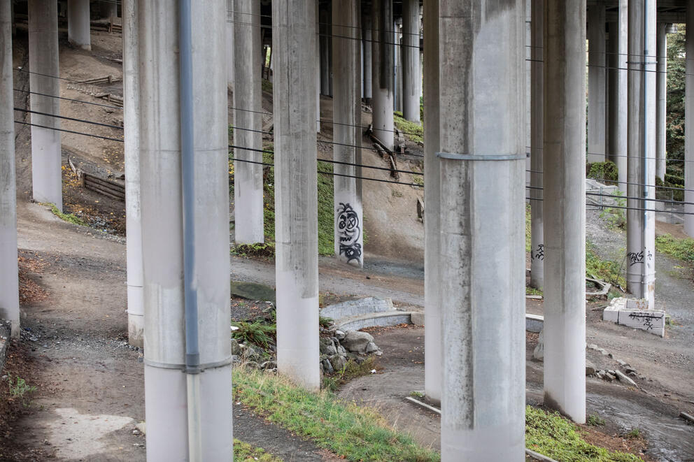 Freshly painted gray colonnades under the freeway frame one at the center that has been tagged with graffiti