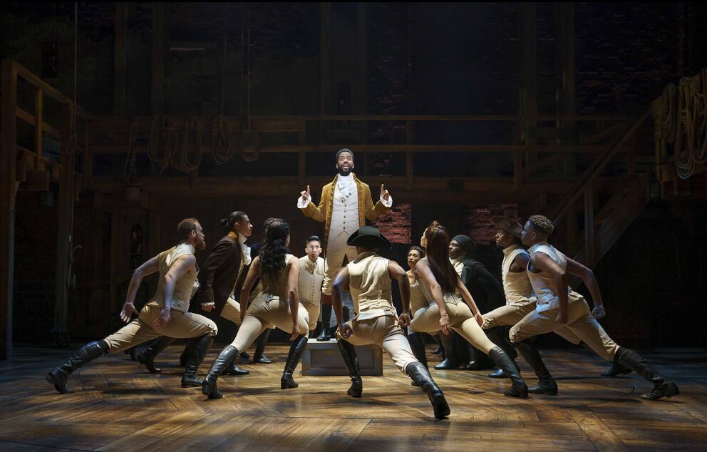 Person on stage in beige clothing surrounded by people