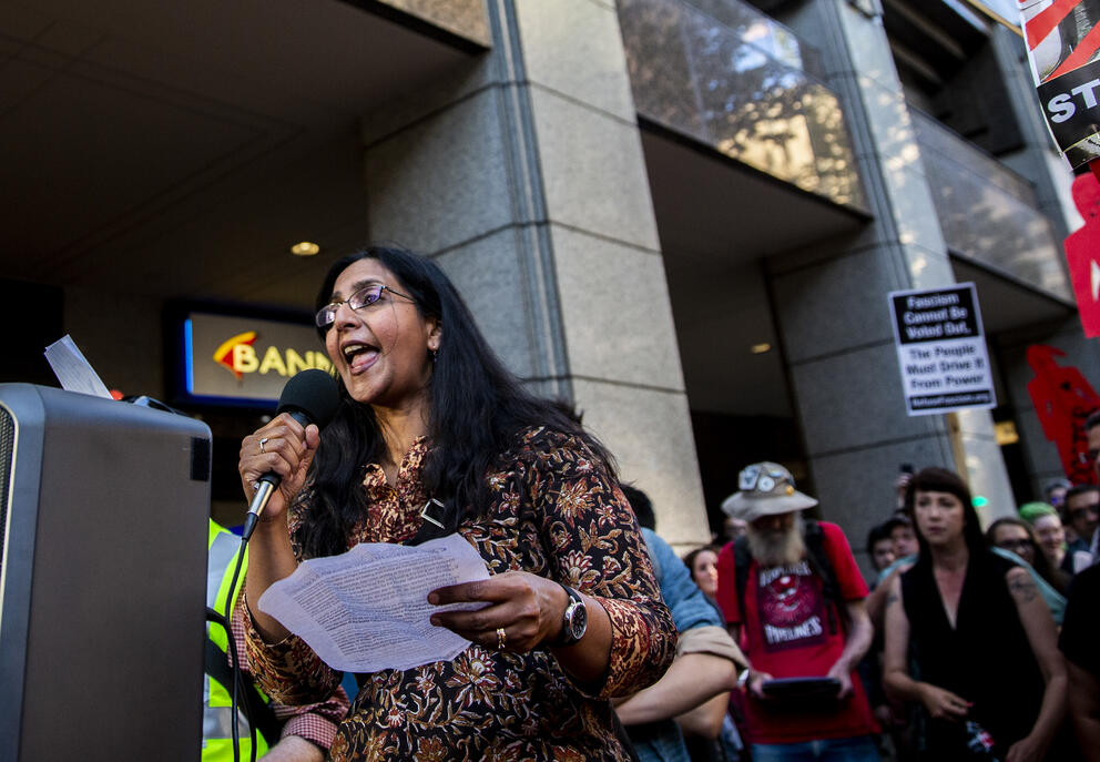 A woman holding a microphone speaks in front of a crowd