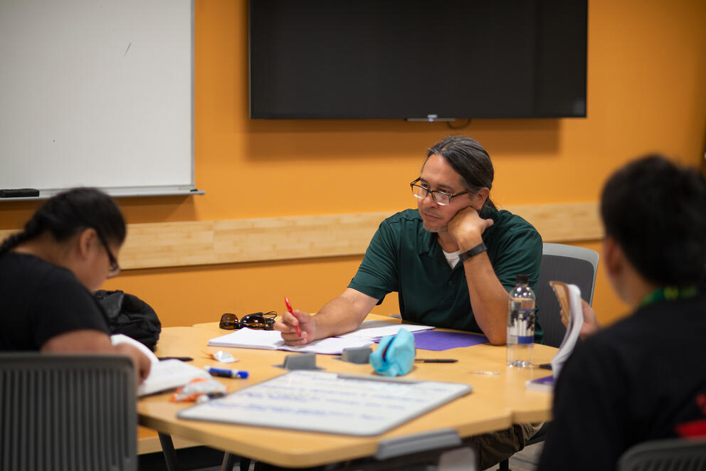Three students sitting together at a desk doing classwork