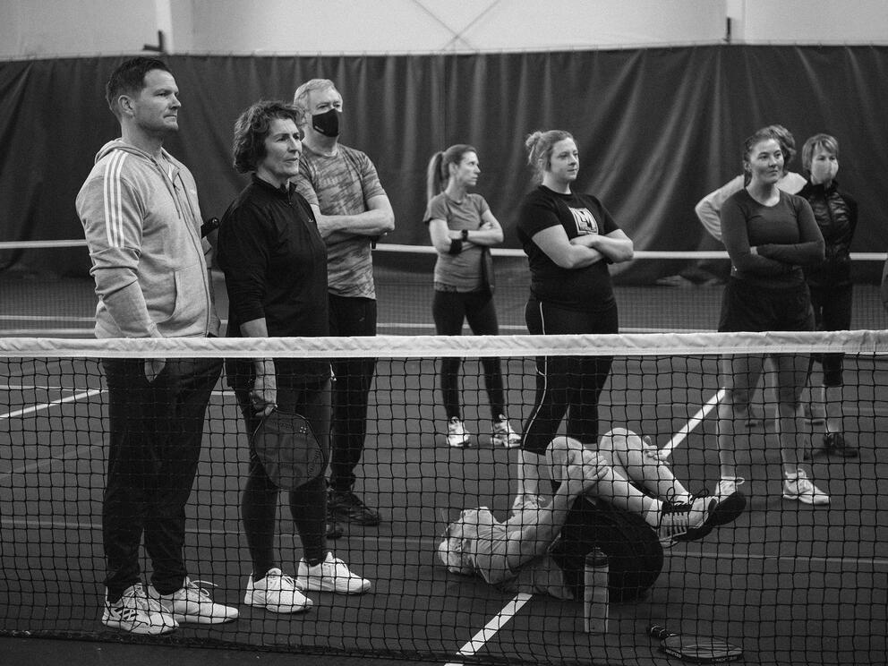pickleball players stand in a group behind a net on an indoor court