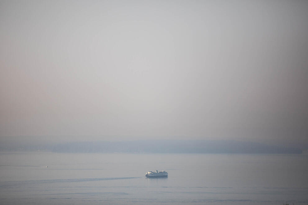 A ferry wades through wildfire smoke in the foreground of mountains 