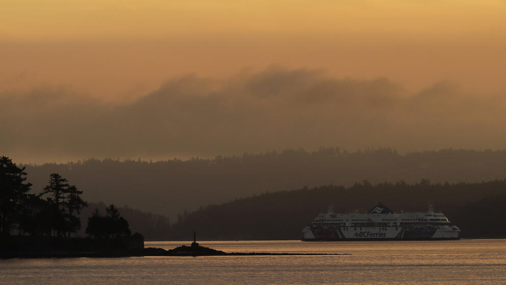 A hazy yellow sky shows shadows of mountains and a ferry boat near Vancouver Island, B.C.