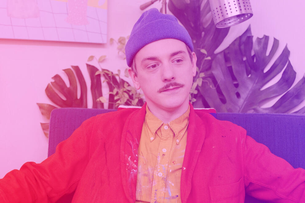 A man sitting down looks off into the distance with a purple/pink filter over him