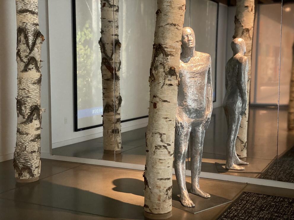 a gallery with a silver humanoid figure standing in a grove of birch trees