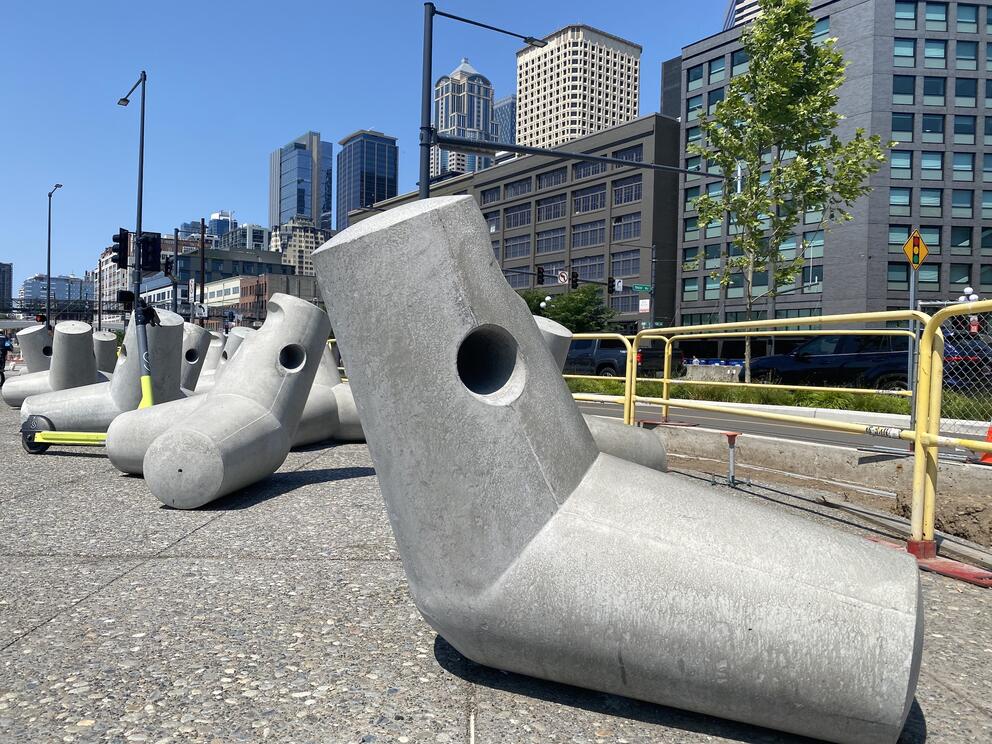 a series of concrete sculptures shaped like jacks with a city skyline behind