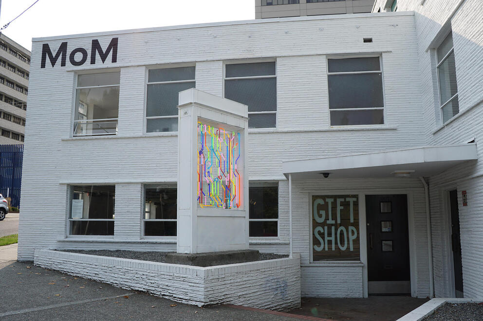 a white midcentury modern building with a neon sculpture in front and the letters MOM at the top