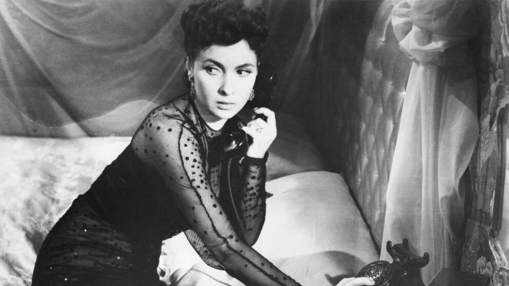 black and white movie still of an elegant 1950s woman calling someone on the phone