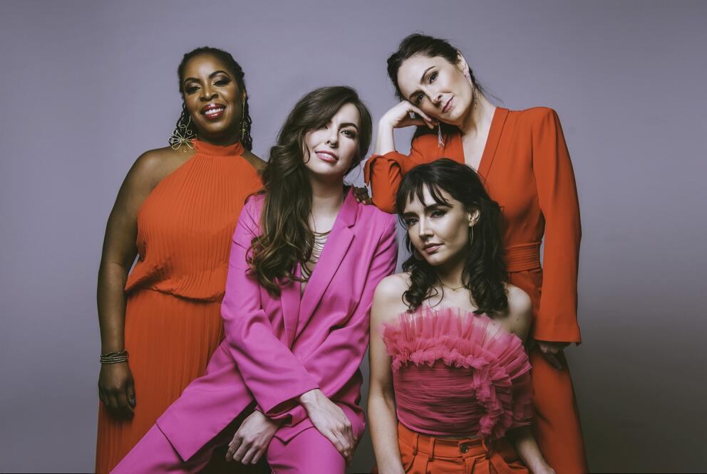 photo of four women standing close together, all wearing shades of pink and red