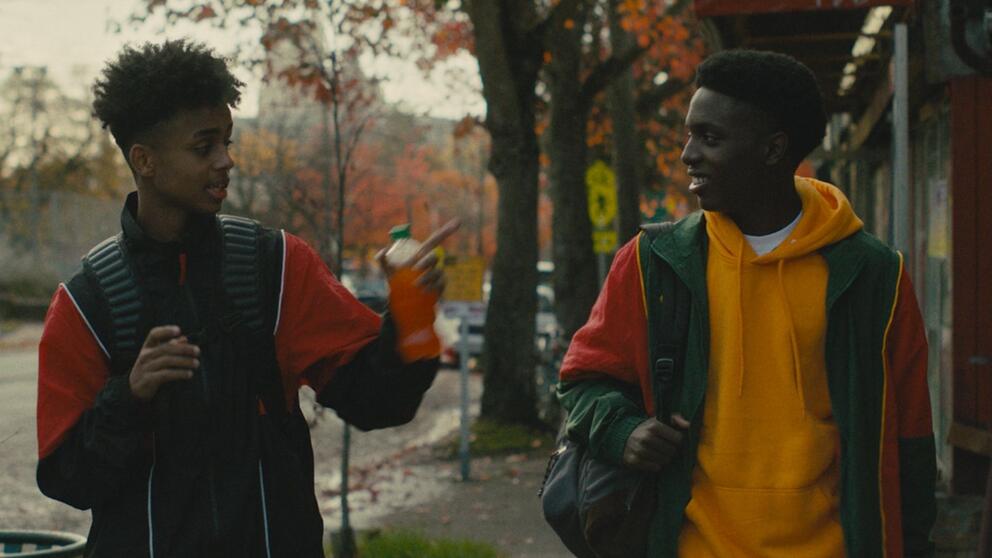 movie still featuring two young black men walking and talking