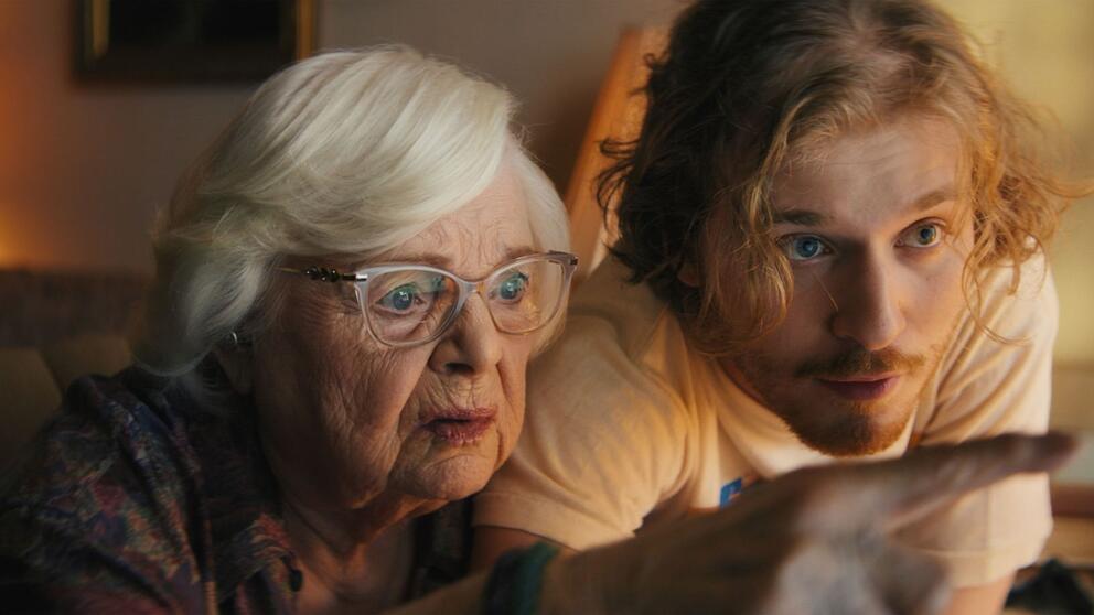 film still featuring a older woman and a grandson leaning over to look at something on a screen