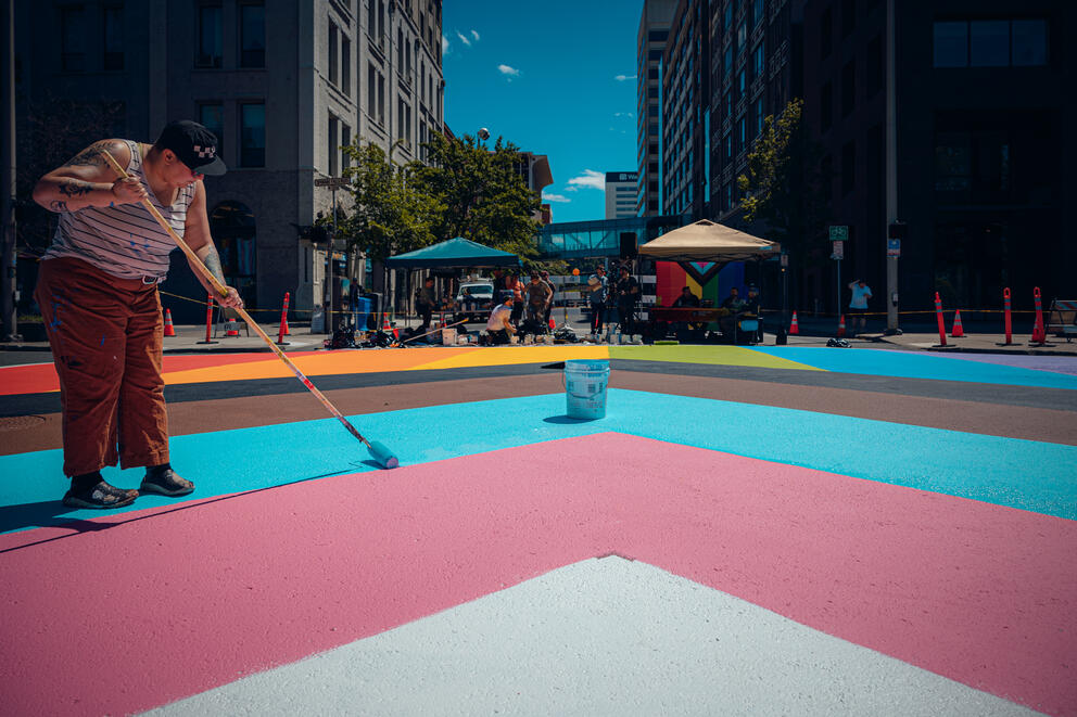 Patterson, a transgender artist, paints the stripes symbolizing the trans community in the Progress Pride flag design.
