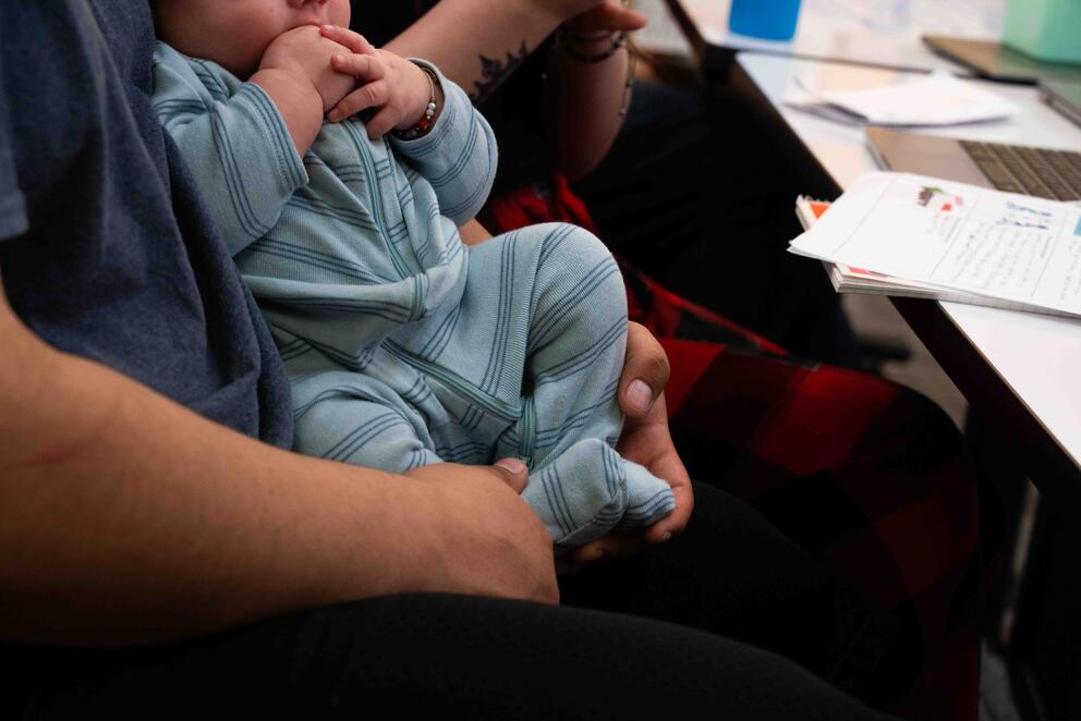 A person is holding a newborn baby at a school desk.