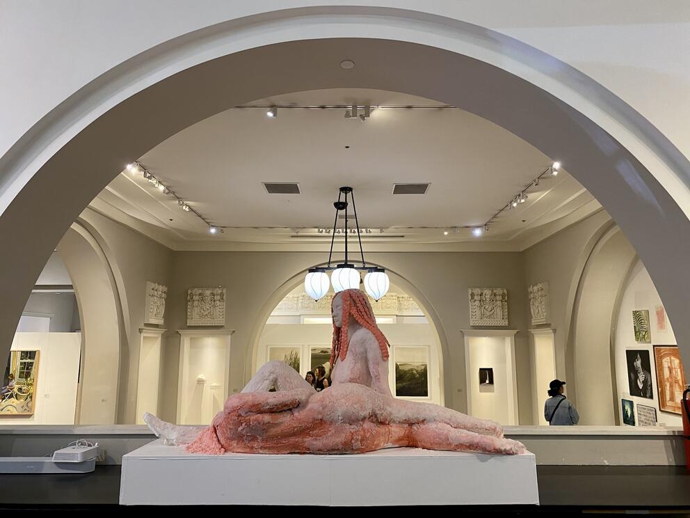 photo of a neoclassical gallery room with a pink sculpture of two women lying down underneath an arched ceiling