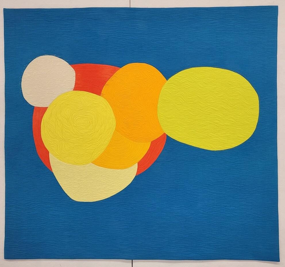 a large abstract quilt featuring orange and yellow orbs on a blue background
