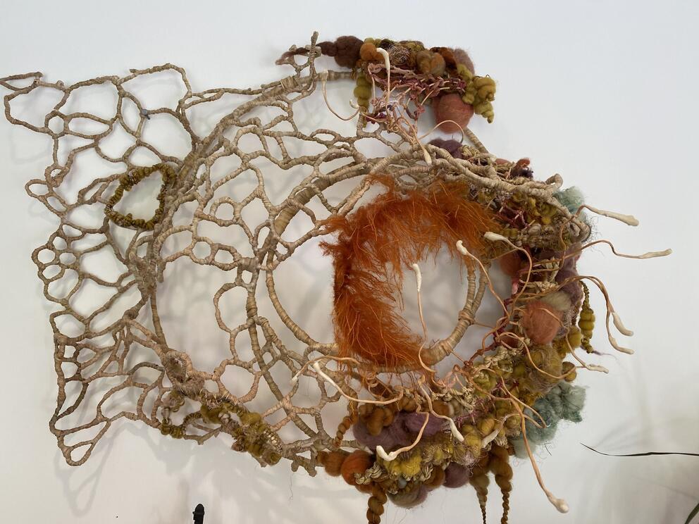 a webby sculpture made of natural fibers with tufts of color