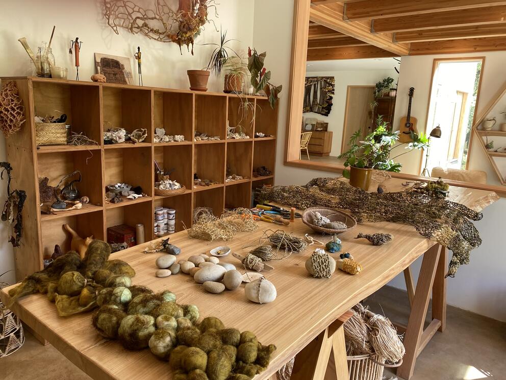 photo of an art studio with shelves and a table full of natural fibers and beach finds