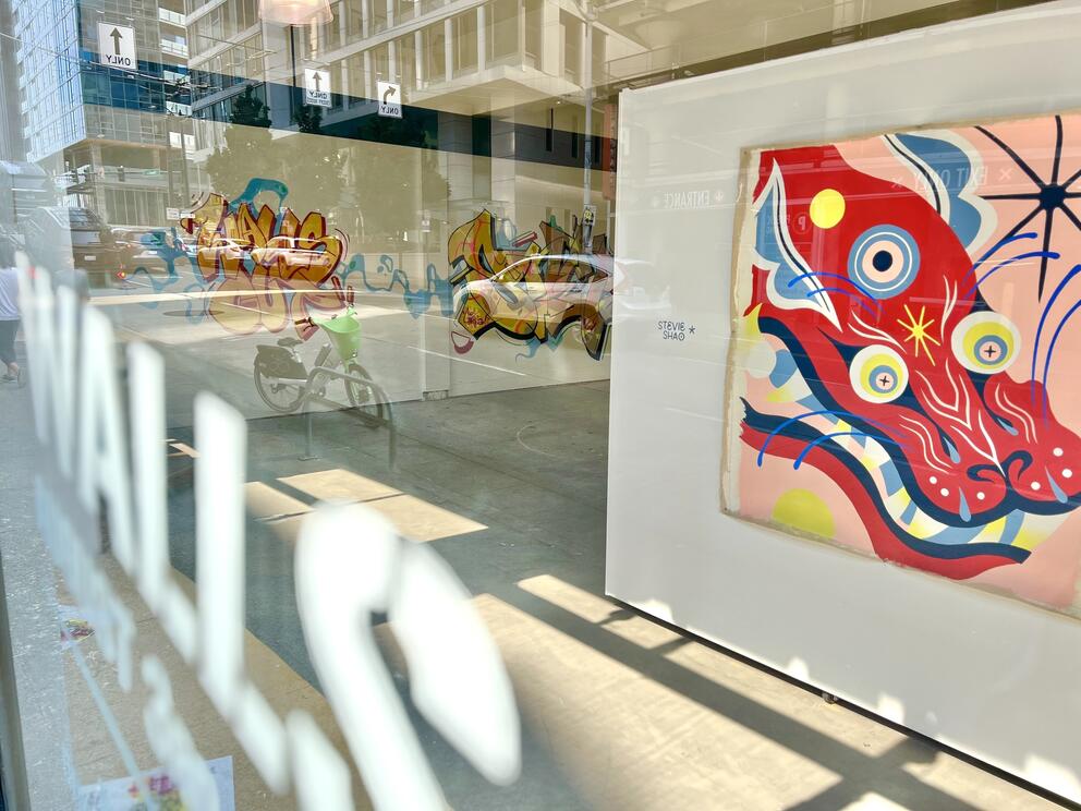 photo from outside peering in thru a gallery window where a large pink-red dragon appears on a wall