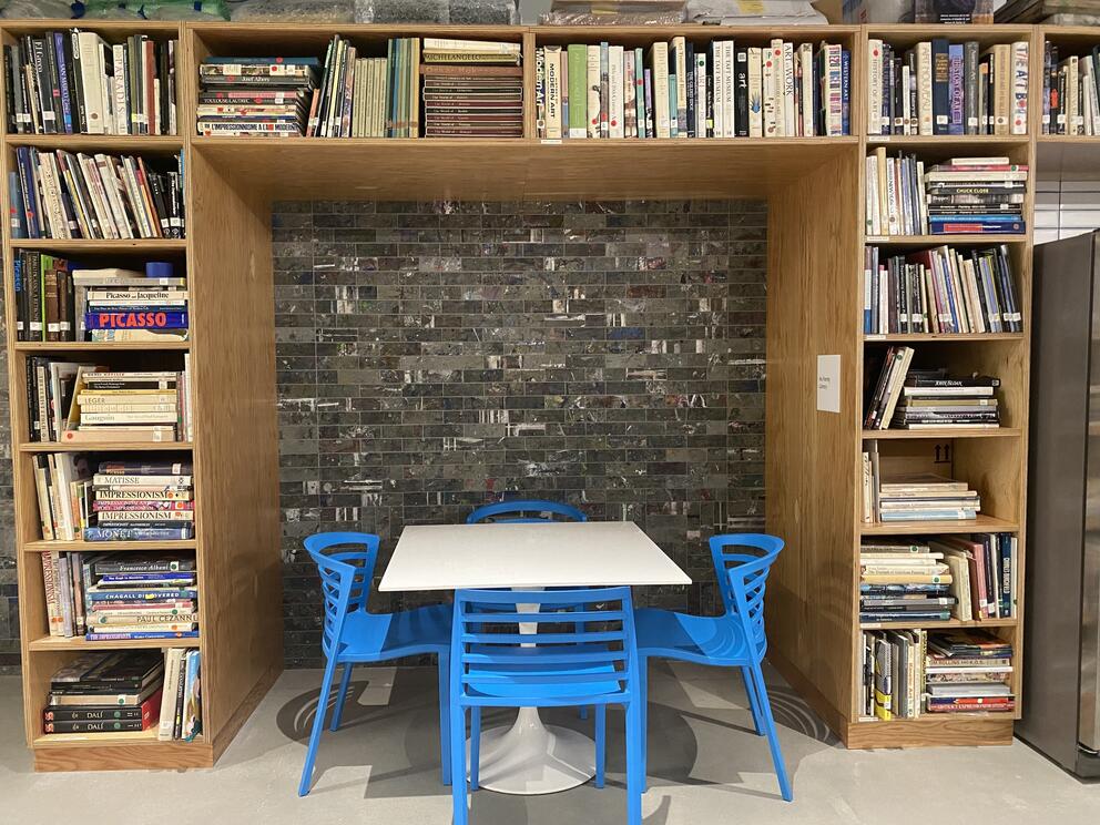 photo of a white table and blue chairs surrounded by bookcases filled with art books