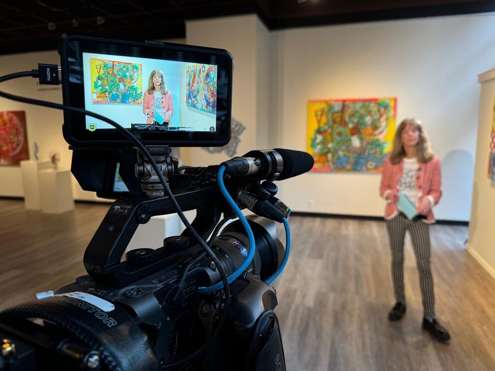 a woman being filmed at an art gallery with camera in the foreground
