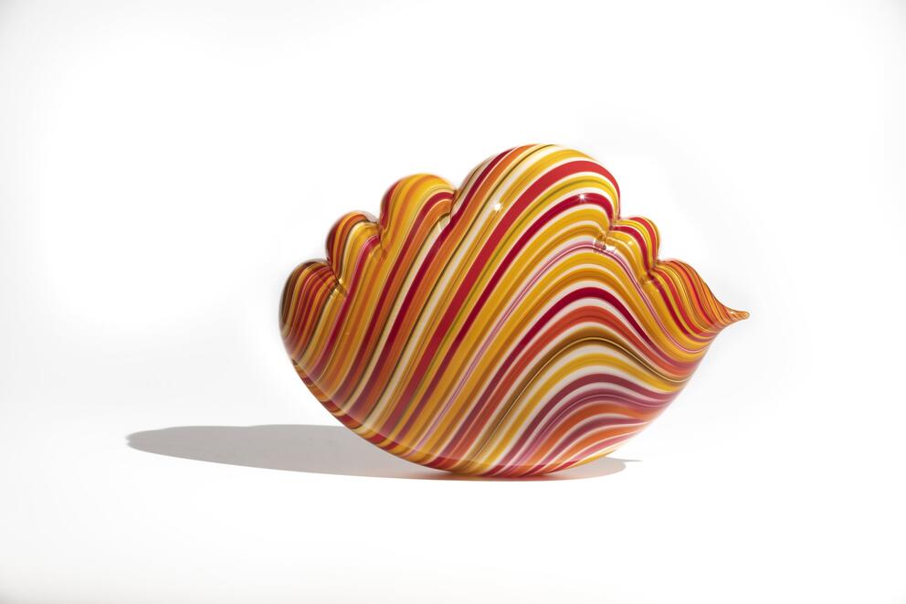 a piece of wavy glass art in stripes of red and orange that looks like a seashell or piece of hard candy