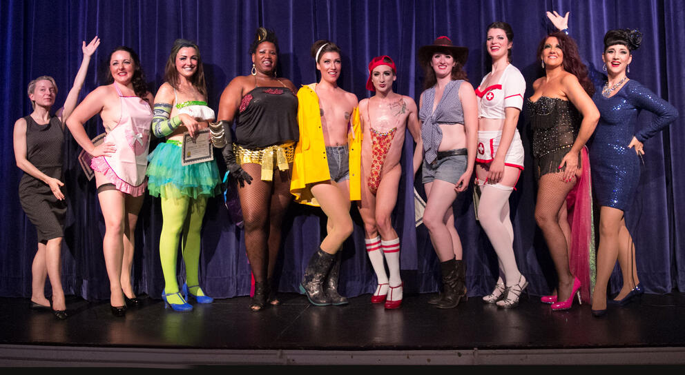Ten burlesque performers in costume pose on stage.