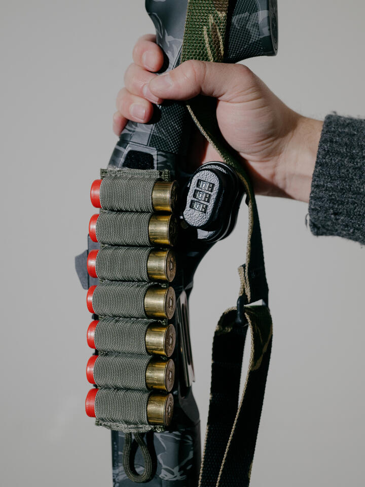 A man's hand holds a shotgun secured with a trigger lock. 