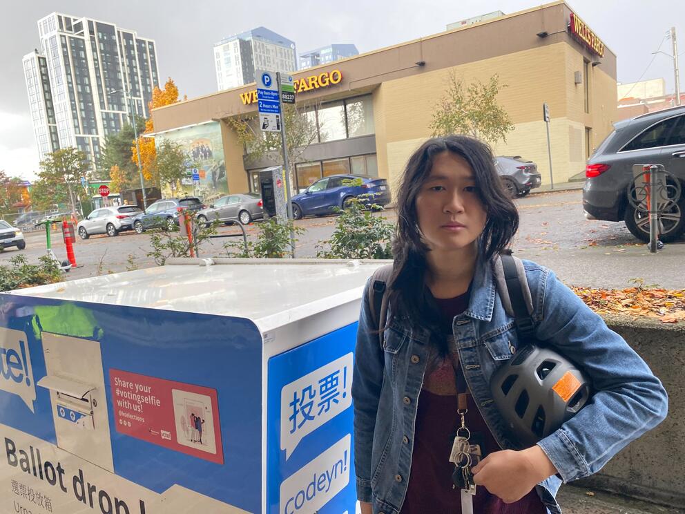 person standing next to a ballot drop box
