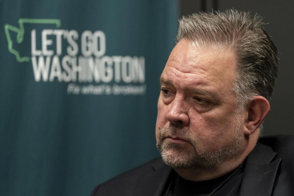 A person sits in front of a backdrop with a logo for "Let's Go Washington."