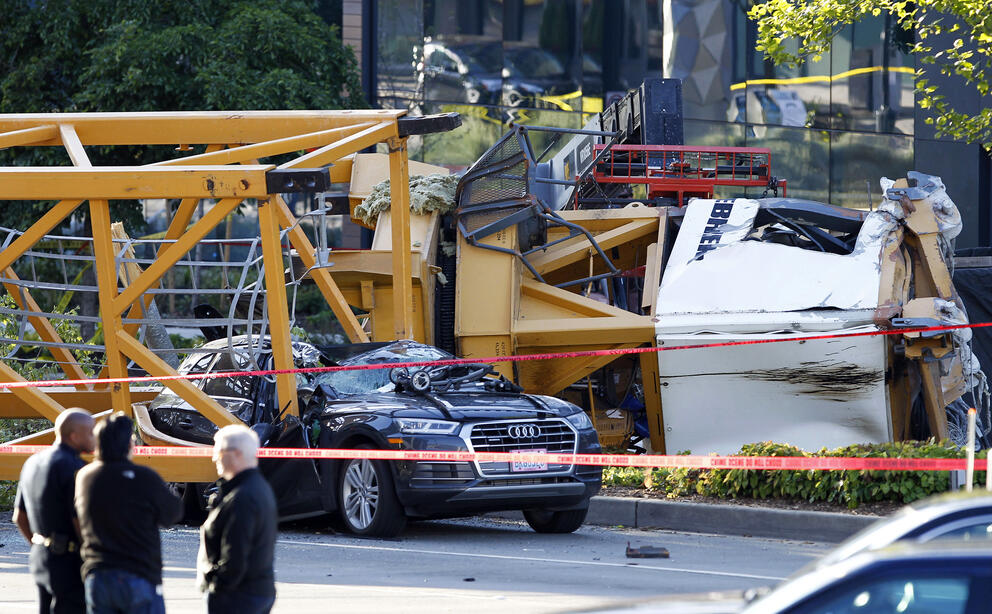 A construction crane is damaged on a street, with parts of the crane on top of an Audi sedan.