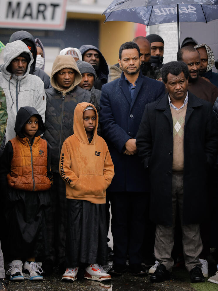 A group of mainly Black men and boys stand together in the rain