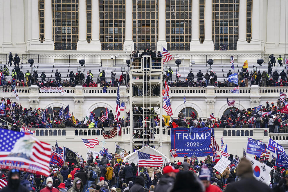 A large number of people crowd the steps and windows outside of the U.S. Capitol building.
