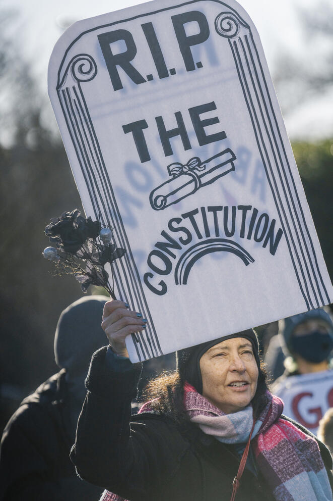 a woman holds a sign reading "RIP the constitution"