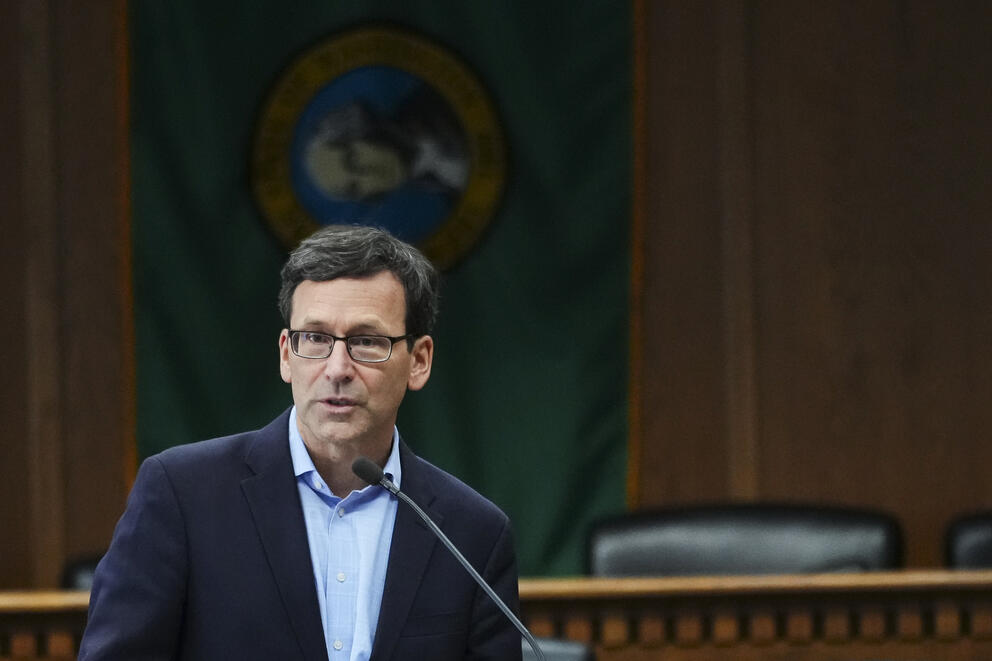 A person stands behind a dais and in front of a Washington state flag.