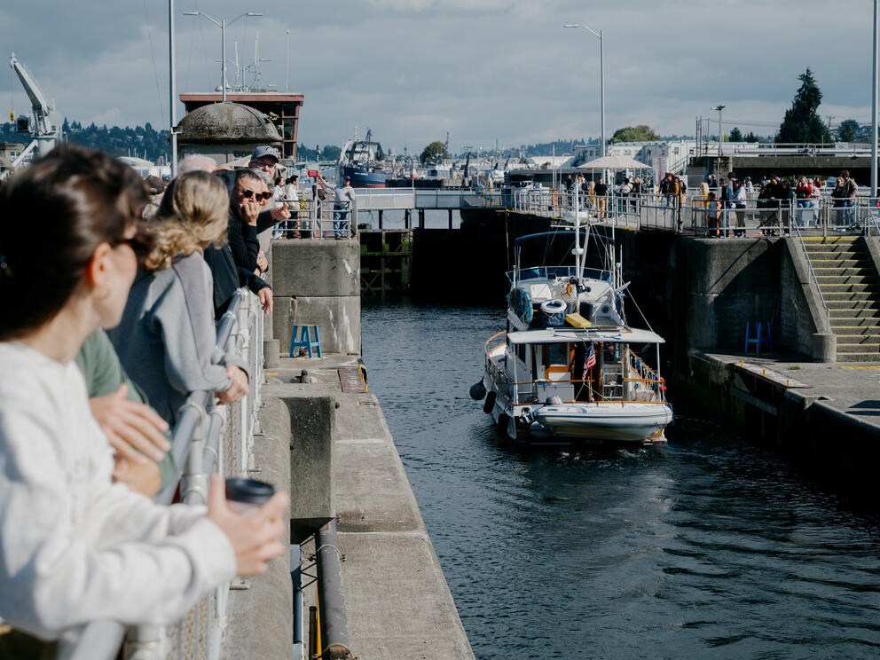 People watch from the edges of the canal as a boat passes through the Ballard locks