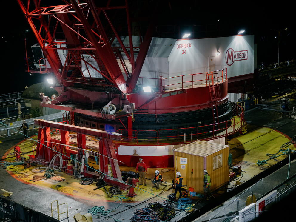 Workers surround the base of a large crane at night