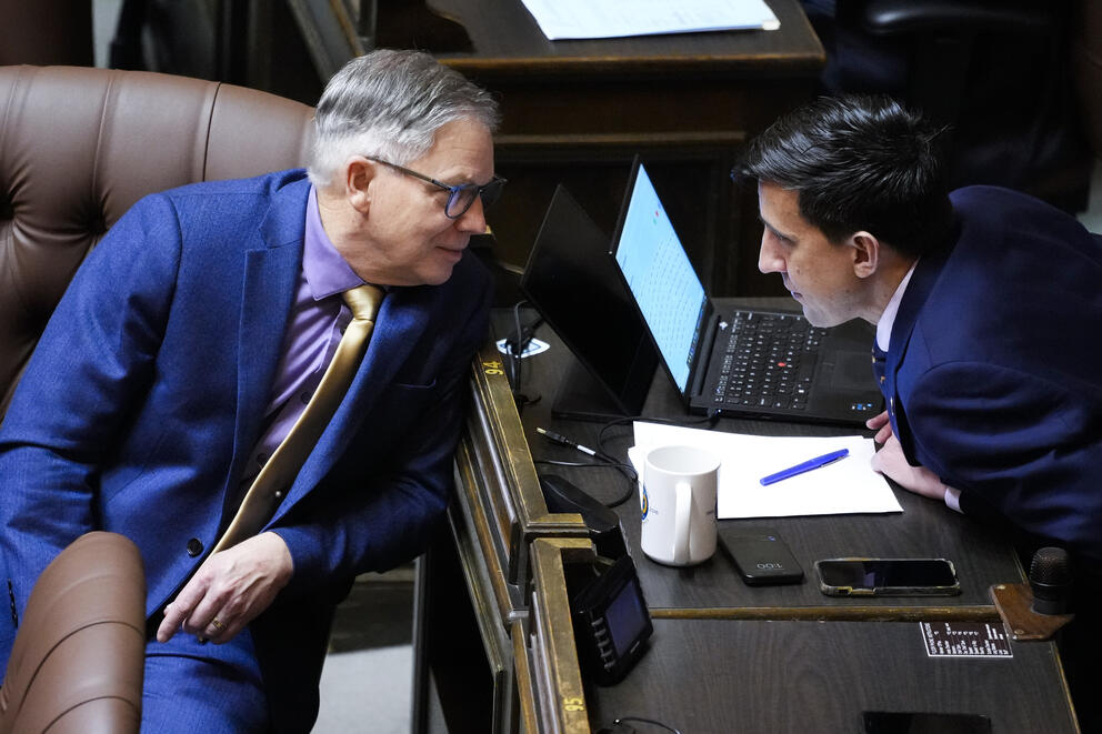 Bill Ramos leans to talk to Alex Ramel on the House chamber floor