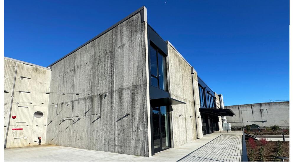 an industrial concrete building with string lights out front, against a blue sky